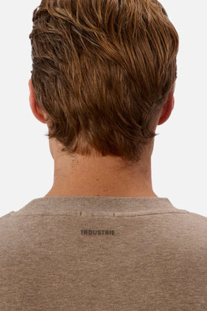 Back view of an individual with light brown hair wearing the Industrie The Newport Tee in gray. "INDUSTRIE" is stylishly printed just below the neckline on this oversized 100% cotton fabric, standing out against a plain white background that emphasizes its minimalist aesthetic.