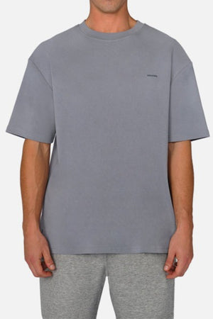 A person wearing Industrie The Newport Tee in a plain gray, featuring an oversized fit and crafted from 100% cotton, stands against a white backdrop. Paired with light gray shorts, the ensemble exudes a casual and relaxed vibe, perfect for effortless style.