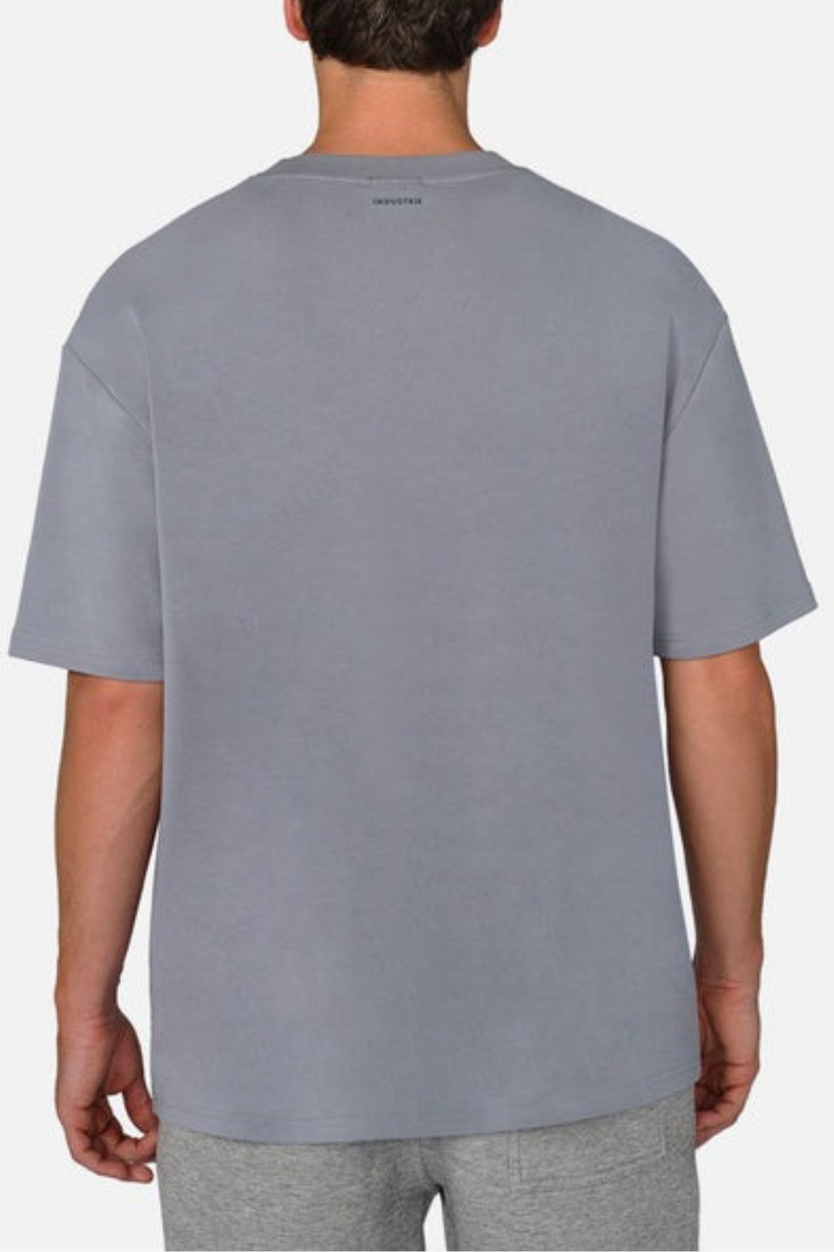 A man stands with his back to the camera against a white background, wearing a gray Industrie The Newport Tee paired with gray shorts. The 100% cotton tee is designed with an oversized fit for enhanced comfort.