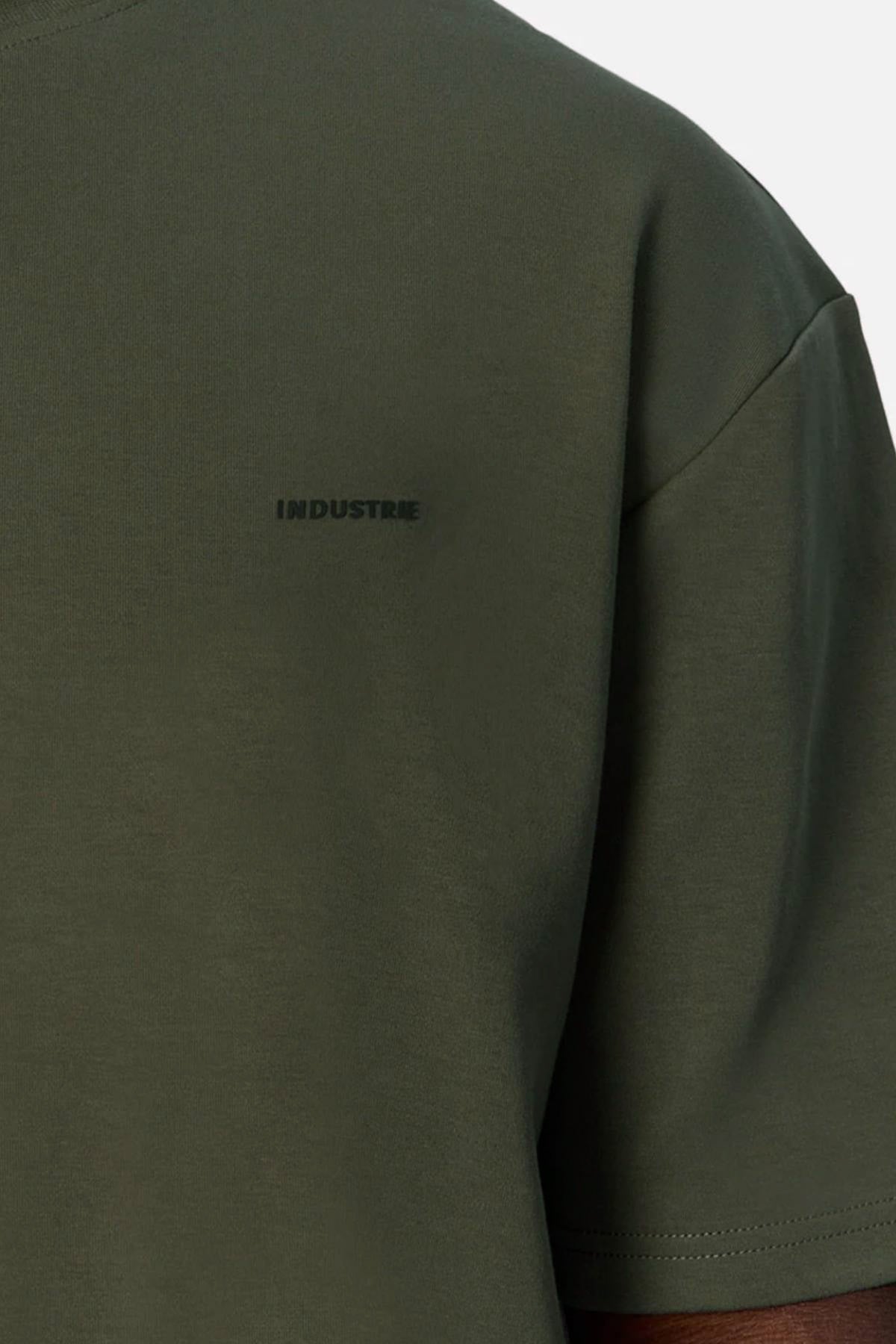 Close-up of a person wearing the olive green Industrie The Newport Tee, featuring "INDUSTRIE" in small dark letters on the left chest. This 100% cotton tee has an oversized fit and is set against a plain light background.