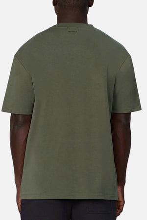 A person is shown from behind wearing an oversized Industrie The Newport Tee in olive green, made of 100% cotton, against a plain light background. The shirt features a simple design with no visible graphics or logos.