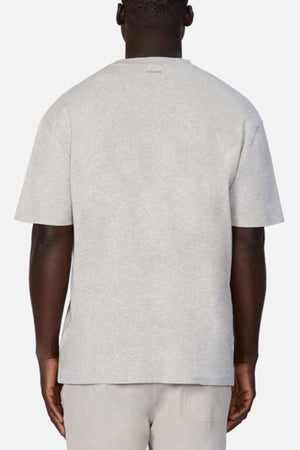 A person wearing an oversized fit of Industrie The Newport Tee in light gray, crafted from 100% cotton, and beige pants is seen from behind against a plain white background.