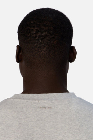 A person with short, dark hair is depicted from behind, dressed in an oversized light gray Industrie The Newport Tee that features "INDUSTRIE" printed on the back. This t-shirt is made entirely of cotton and set against a plain white background.