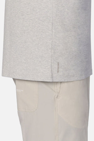The image showcases a side view of an individual wearing Industrie The Newport Tee in light gray, alongside beige pants. This angle emphasizes the textures and materials of the 100% cotton garment, featuring an oversized fit.
