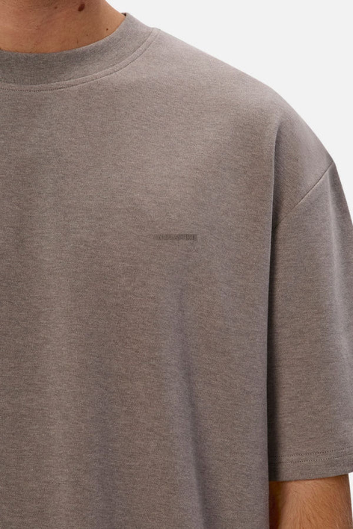 A person wears an Industrie The Newport Tee in a plain gray, short sleeve style. Crafted from 100% cotton, this T-shirt includes a small, subtle logo on the chest. The white background emphasizes its casual yet sophisticated look as the image focuses on the upper torso.