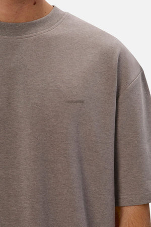 A person wears an Industrie The Newport Tee in a plain gray, short sleeve style. Crafted from 100% cotton, this T-shirt includes a small, subtle logo on the chest. The white background emphasizes its casual yet sophisticated look as the image focuses on the upper torso.