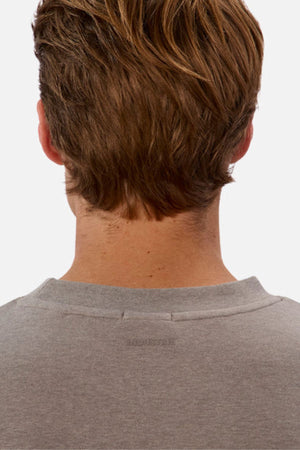 The image features the back of a person's head with light brown hair, wearing an oversized gray shirt—Industrie The Newport Tee, made from 100% cotton. The background is a plain white.