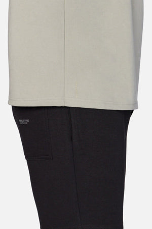 A close-up side view shows someone in an oversized fit light gray shirt with black pants, displaying "INDUSTRIE RECINE" above a small pocket. The focus is on heavyweight fabric and overlapping layers, echoing the style of Industrie's The Newport Tee.
