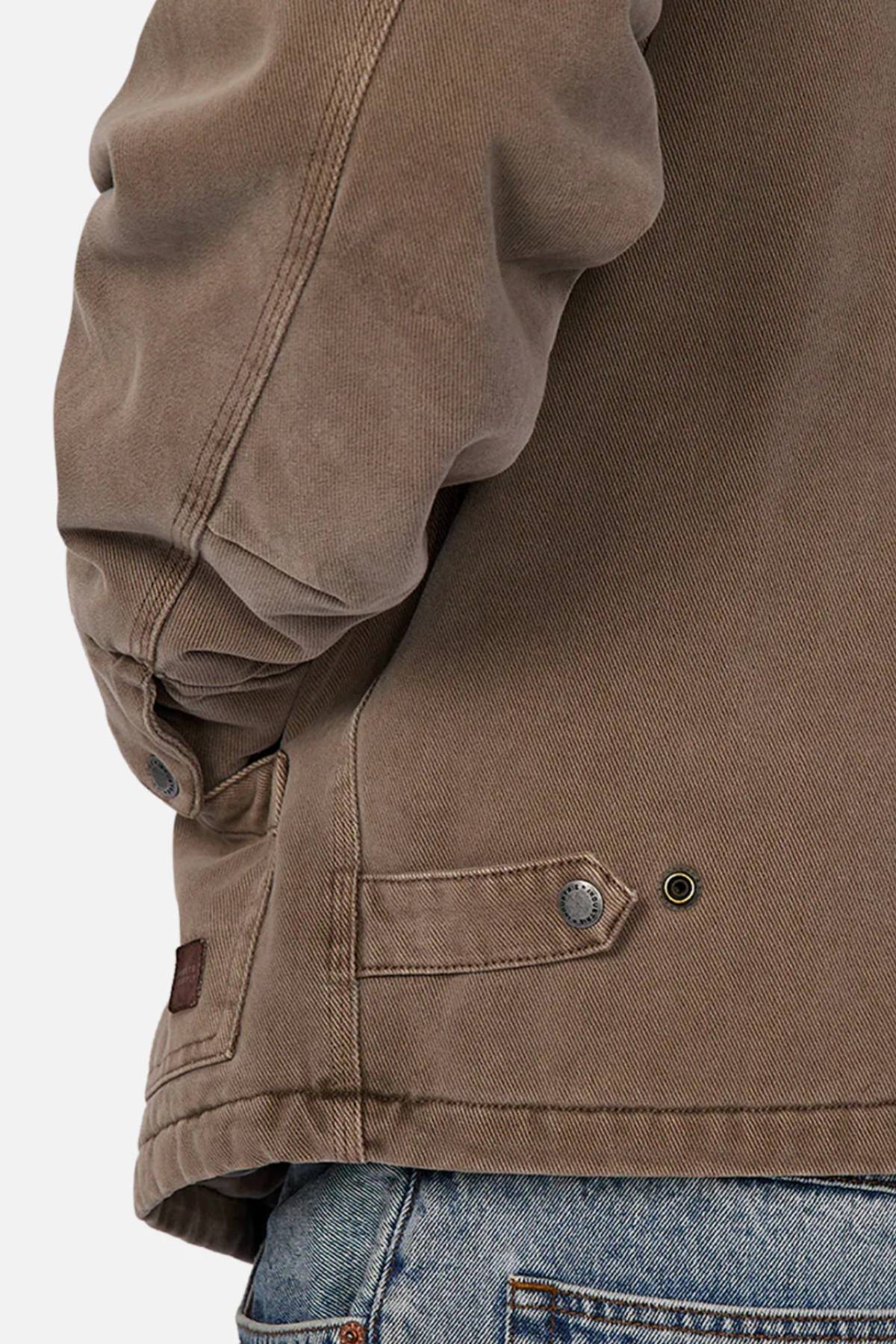 A close-up of a person wearing the Industrie The Oklahoma Jacket, a casual-fit outerwear piece with adjustable side tabs, shown paired with blue denim jeans. The image highlights the lower back and arm of this versatile jacket.