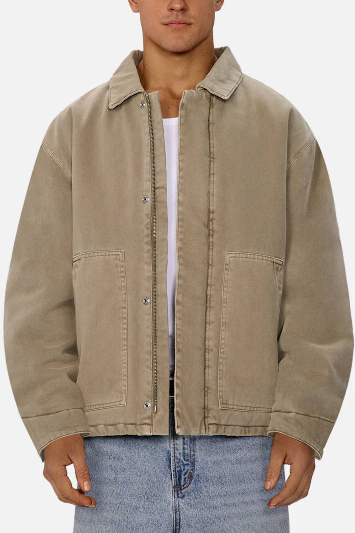 Wearing the Industrie The Oklahoma Jacket in tan over a white shirt and blue jeans, a person stands against a plain light background. This casual-fit jacket features a collar, metal snap buttons, front pockets, and functional design details.