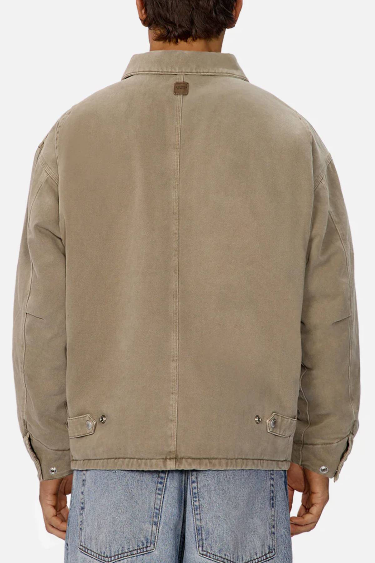 A person wears the Industrie The Oklahoma Jacket in light brown with a relaxed fit and back button details, paired with light blue jeans, viewed from behind against a plain, light background.