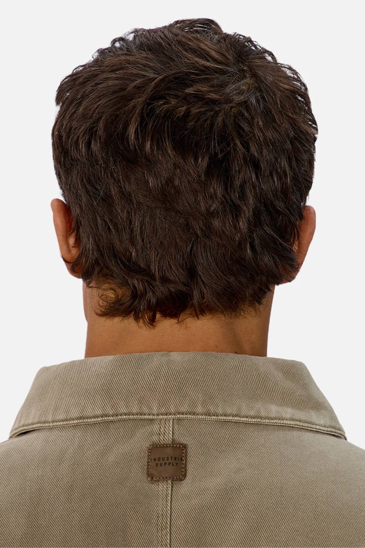 The image shows the back of a person's head with short, wavy brown hair, wearing the Industrie The Oklahoma Jacket. A small brown rectangular label on the back collar highlights the jacket’s practical design.