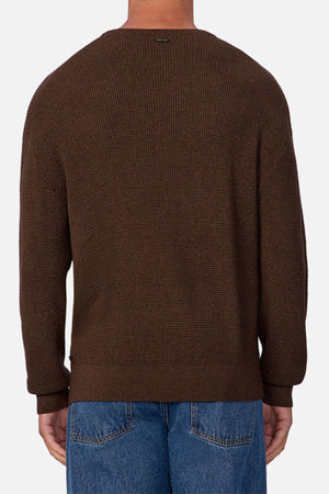 A person is shown from the back against a plain white background, wearing Industrie The Philly Waffle Knit sweater in textured brown and blue jeans.