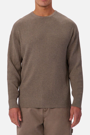 Someone is wearing the Industrie The Philly Waffle Knit, a textured long-sleeve crew neck sweater in light brown, paired with matching pants and standing against a plain light background.
