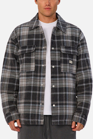 Someone wears the Industrie The Phoenix Jacket—a plaid shirt jacket in gray, black, and white with a heavyweight feel—over a white T-shirt and dark pants, standing against a plain background.