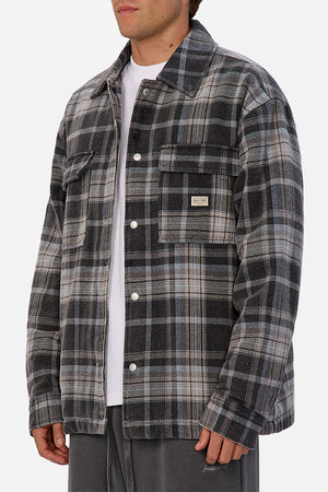 Someone wearing the Industrie The Phoenix Jacket—a gray and black plaid heavyweight shirt jacket—over a white t-shirt and gray pants, standing against a plain white background.