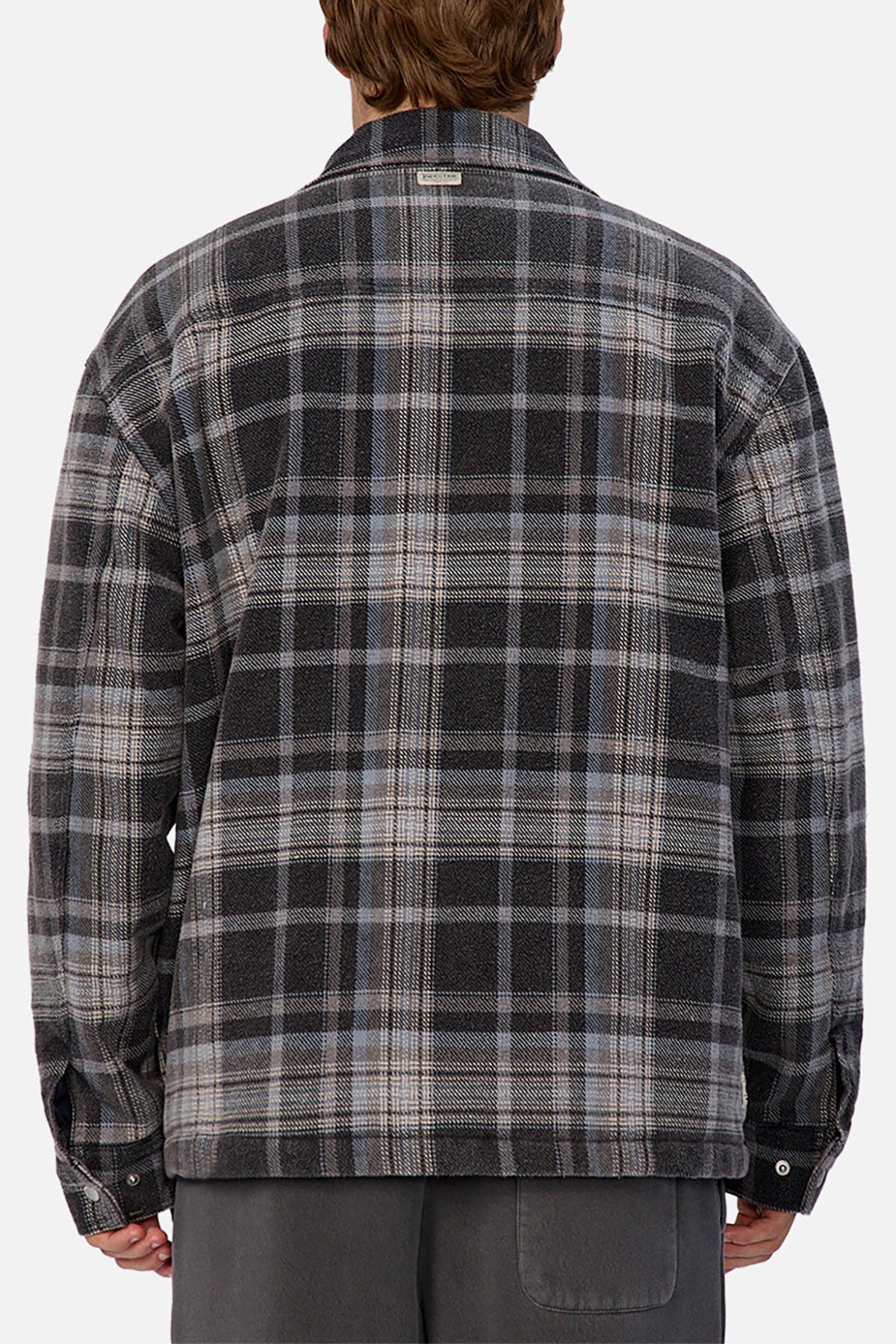 A person facing away from the camera wears the Industrie The Phoenix Jacket, a gray and black plaid heavyweight shirt jacket with long sleeves, paired with dark gray pants.