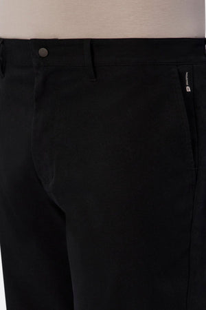 Close-up of a person wearing Industrie The Tech Pinehurst Chino Pant in black. The smooth fabric, crafted from recycled polyester for extra flexibility, features a small visible zipper on the side. Belt loops and a single button closure accentuate the garment's design against a neutral background.