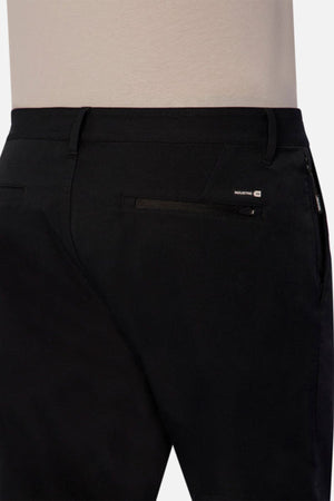 A person wearing black Industrie The Tech Pinehurst Chino Pant, which includes a zipper pocket on the back right side. These pants showcase a subtle logo patch above the pocket and provide exceptional flexibility due to their recycled polyester fabric.