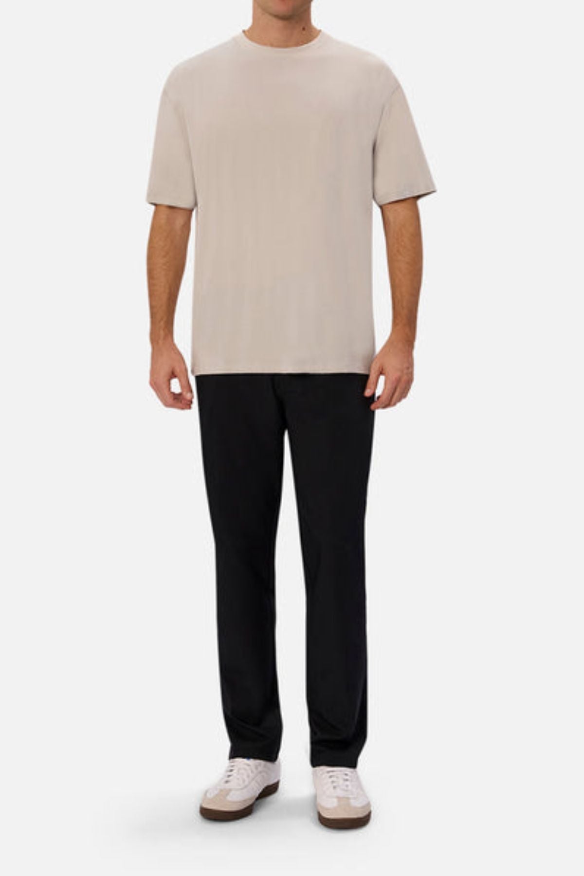 A person wearing a beige T-shirt, Industrie The Tech Pinehurst Chino Pant, and white sneakers stands against a plain white background. The casual outfit, featuring recycled polyester for added flexibility, is minimalistic yet sophisticated.