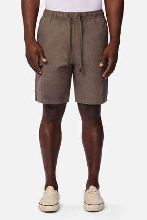 A person wearing an Industrie white shirt, Industrie The Platoon Combat Short in taupe with an elastic waistband, and beige sneakers stands against a plain white background.