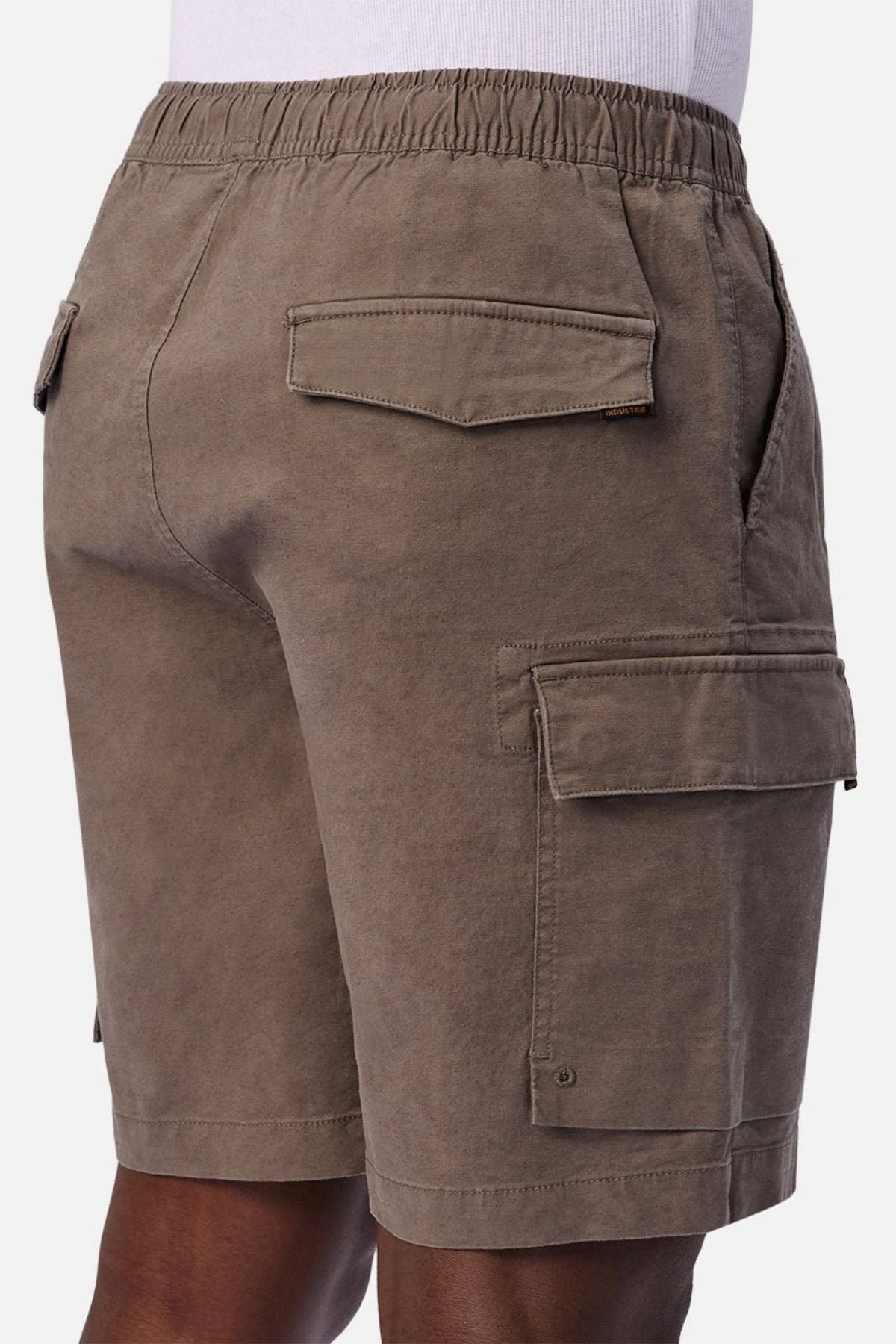 A person standing sideways from waist to knee against a white background is wearing the Industrie The Platoon Combat Short in brown, featuring an elastic waistband as well as side and back pockets.
