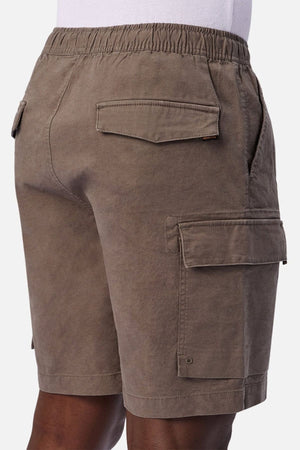 A person standing sideways from waist to knee against a white background is wearing the Industrie The Platoon Combat Short in brown, featuring an elastic waistband as well as side and back pockets.