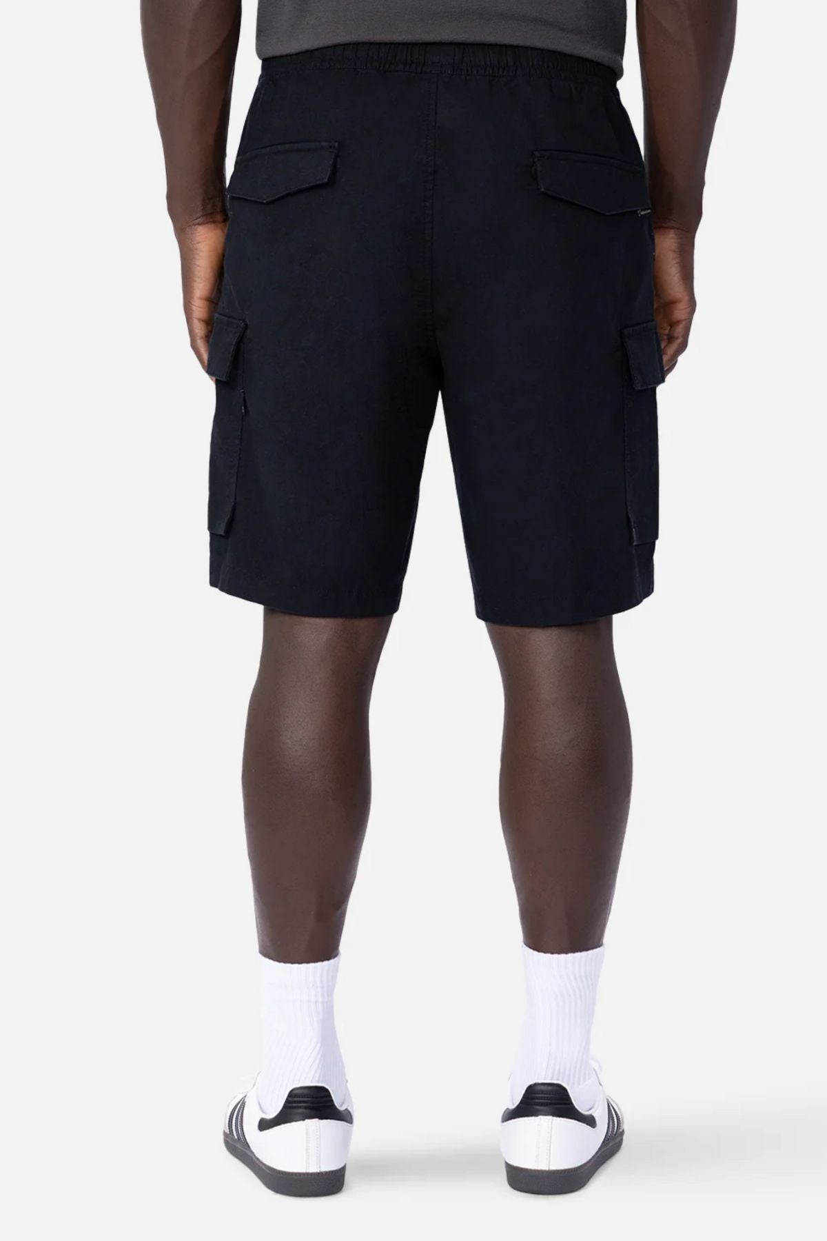 A person is seen from the back against a plain light gray background wearing Industrie The Platoon Combat Short in black, paired with white crew socks and white slide sandals.