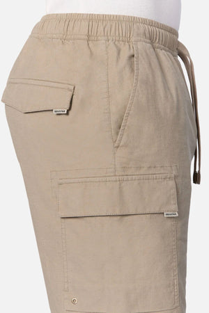 A close-up side view of a person wearing Industrie The Platoon Combat Short in light brown, featuring an elastic waistband, drawstring, and four practical flap pockets.