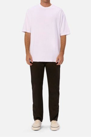 A person faces forward, wearing a plain white oversized T-shirt, Industrie The Regular Cuba Chino Pant with a wider leg fit, and light sneakers against a plain white background. The person's face is not visible.