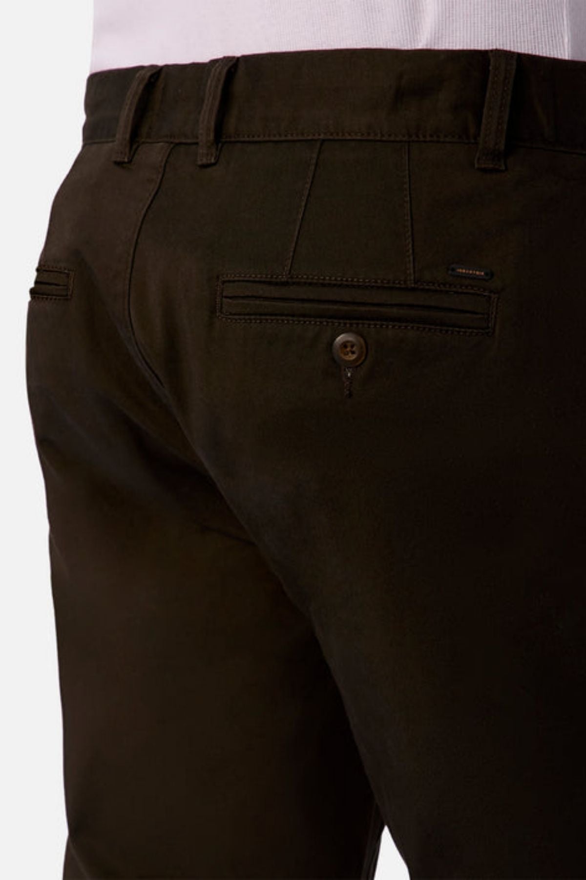 A close-up of someone wearing Industrie The Regular Cuba Chino Pant in dark brown stretch cotton, paired with a tucked-in white shirt, highlights the waistband, belt loops, and buttoned back pocket.