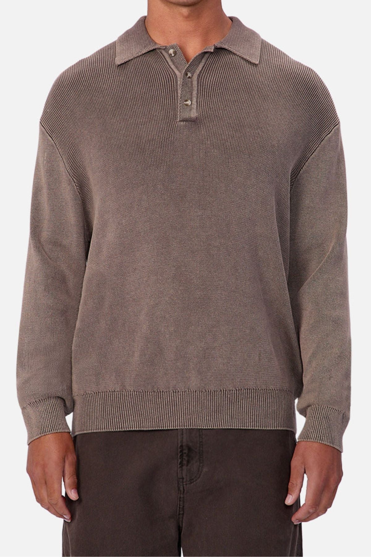 A person wearing the Industrie The Sawtelle Knit—a loose-fitting, long-sleeved polo sweater with a classic collar and three buttons—paired with dark brown pants stands against a plain light background.