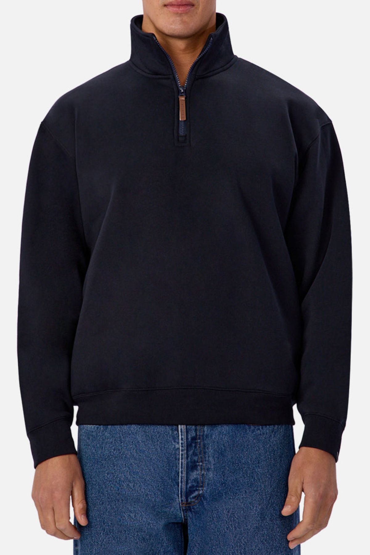 A person in an Industrie The Staunton Track Top—a black quarter-zip pullover sweater—and blue jeans stands against a plain light background.