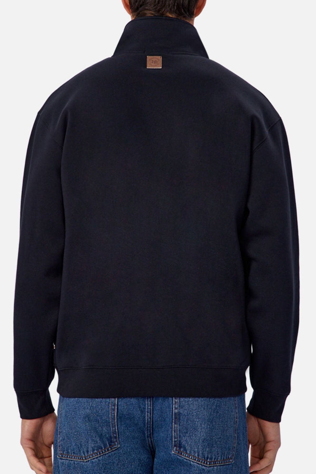 A person is shown from the back against a plain light background, wearing blue jeans and Industrie The Staunton Track Top, which features a small brown patch near the collar.
