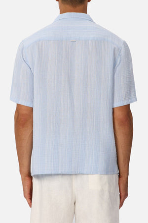 A person is shown from the back against a plain, light background wearing the Industrie The Striped Seguro Short Sleeve Shirt in light blue with white pants.