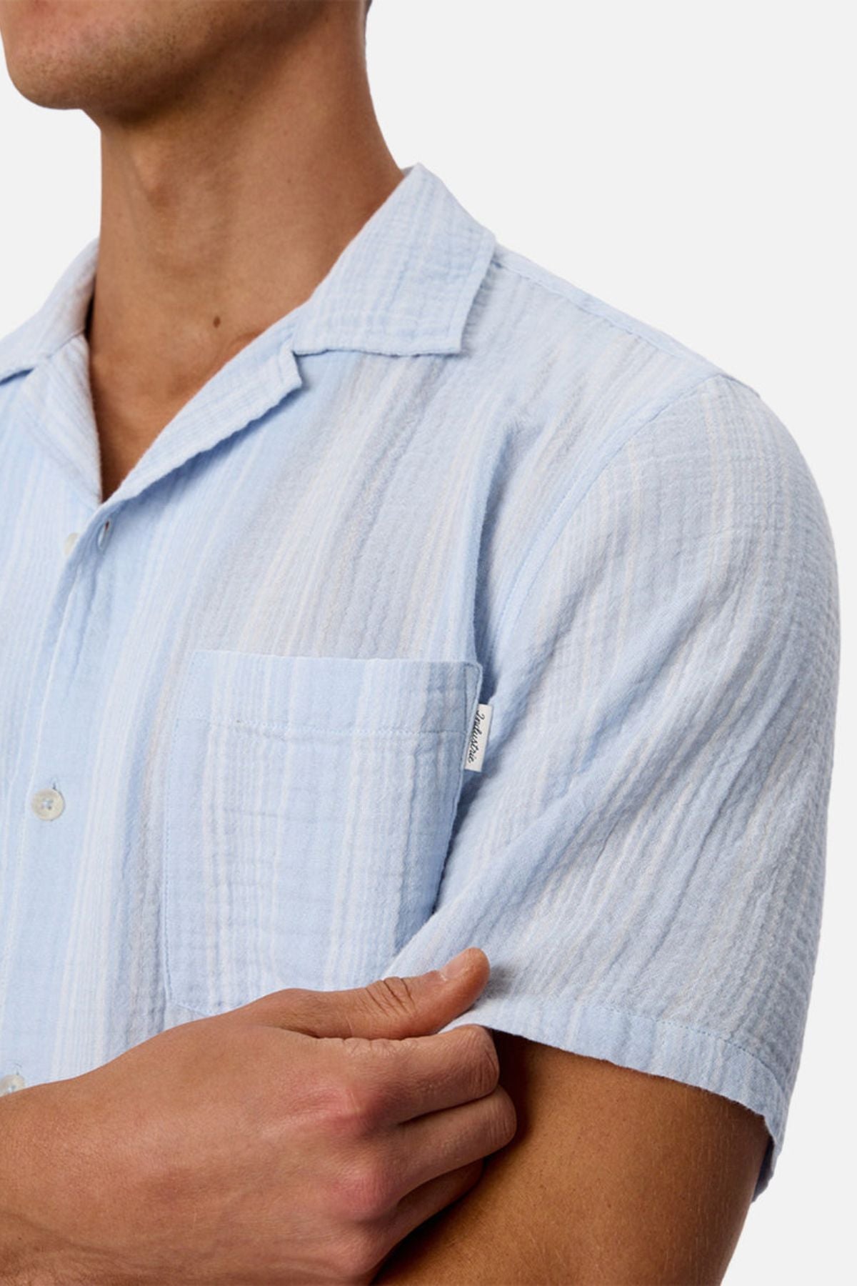 A person wearing the Industrie The Striped Seguro Short Sleeve Shirt, featuring light blue stripes, short sleeves, and a chest pocket, is shown from shoulders to waist with arms crossed against a plain background.