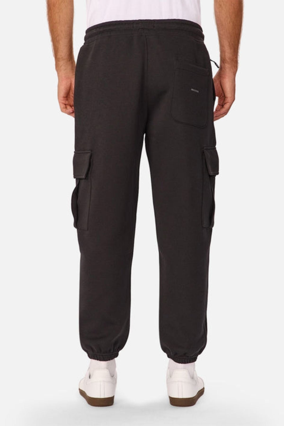Back view of a person wearing Industrie The Tech Combat Trackpant in black with a customizable fit, side and back pockets, paired with a white shirt and sneakers, standing against a plain background.