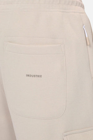 Close-up of the back pocket on Industrie The Tech Combat Trackpant in beige, with "INDUSTRIE" printed above the pocket and a white zipper pull by the side seam, showcasing its modern athletic performance style.