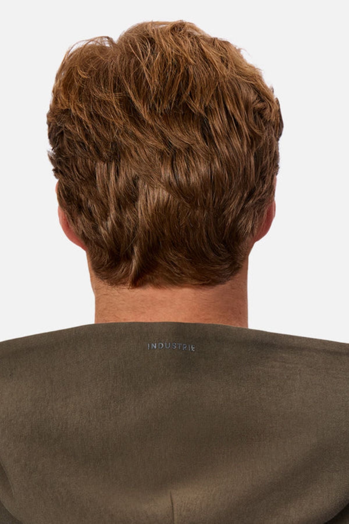 Seen from behind against a plain white background, a person with short, wavy light brown hair wears the Industrie The Tech Del Sur Hood in olive green, which displays "INDUSTRIE" in high density print on the back collar.