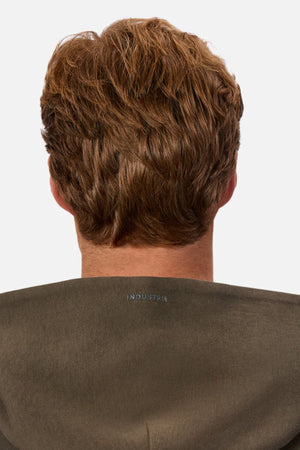 Seen from behind against a plain white background, a person with short, wavy light brown hair wears the Industrie The Tech Del Sur Hood in olive green, which displays "INDUSTRIE" in high density print on the back collar.