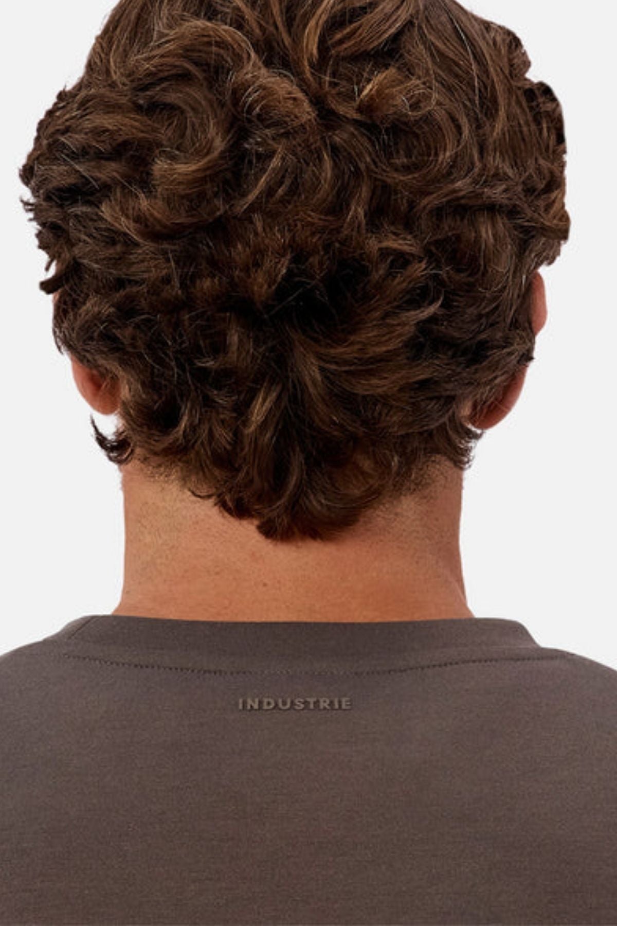 A person with short, curly brown hair is seen from behind wearing the Industrie The Tech Del Sur Sweat, a dark grey modern athleisure top made from comfortable 4-way stretch fabric and featuring "INDUSTRIE" subtly on the collar.