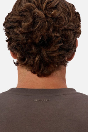 A person with short, curly brown hair is seen from behind wearing the Industrie The Tech Del Sur Sweat, a dark grey modern athleisure top made from comfortable 4-way stretch fabric and featuring "INDUSTRIE" subtly on the collar.