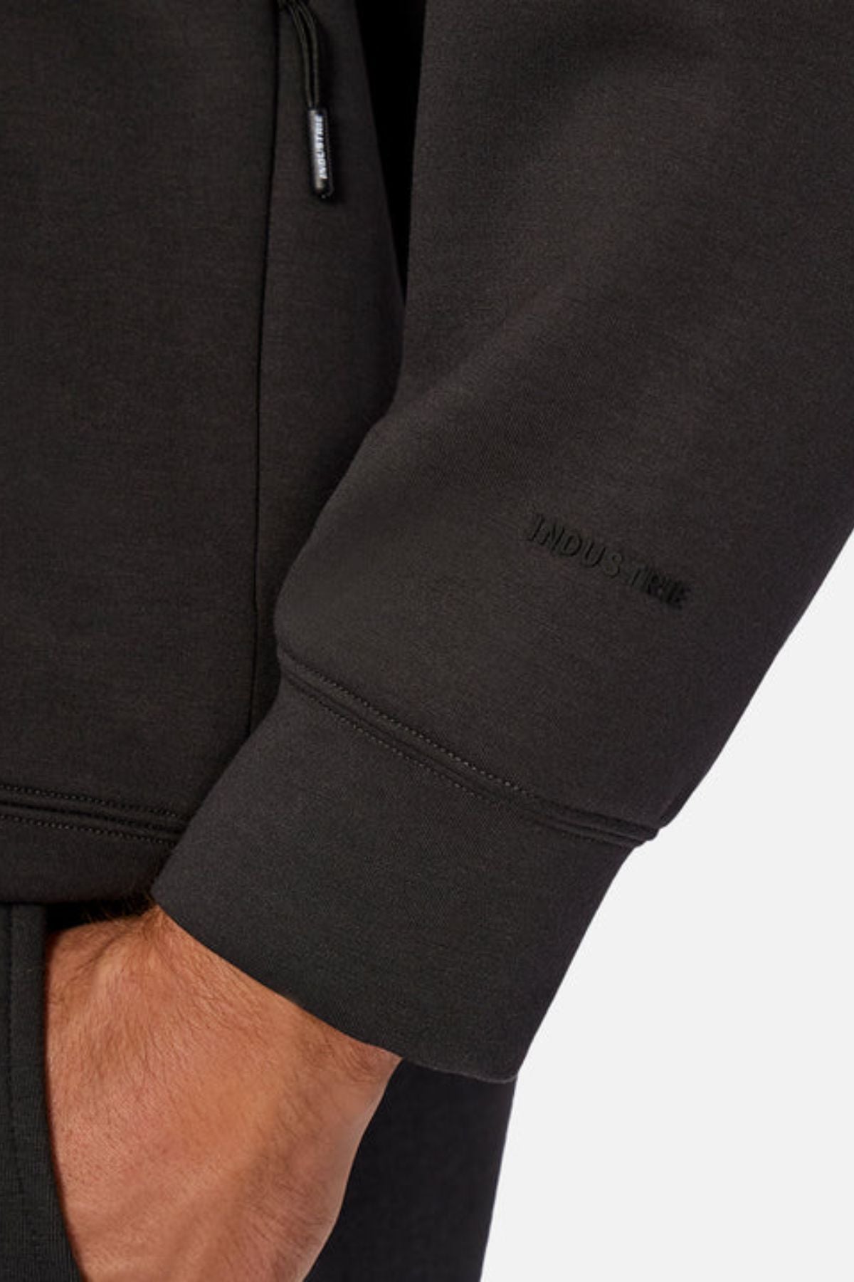 Close-up of a person wearing the Industrie The Tech Del Sur Sweat, which has 4-way stretch fabric and subtle "INDUSTRIE" branding near the black sleeve’s wrist, shown against a plain, light background.