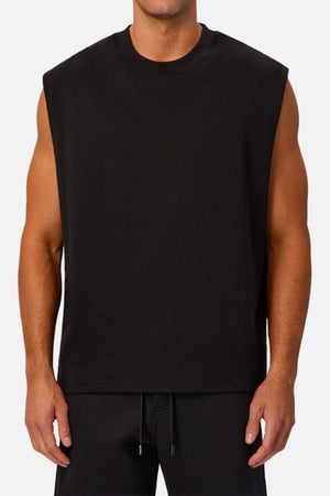 A man wearing the Industrie The Tech Port Sleeveless Tee and black pants stands against a plain light background. His arms are relaxed at his sides, and his face is not visible.
