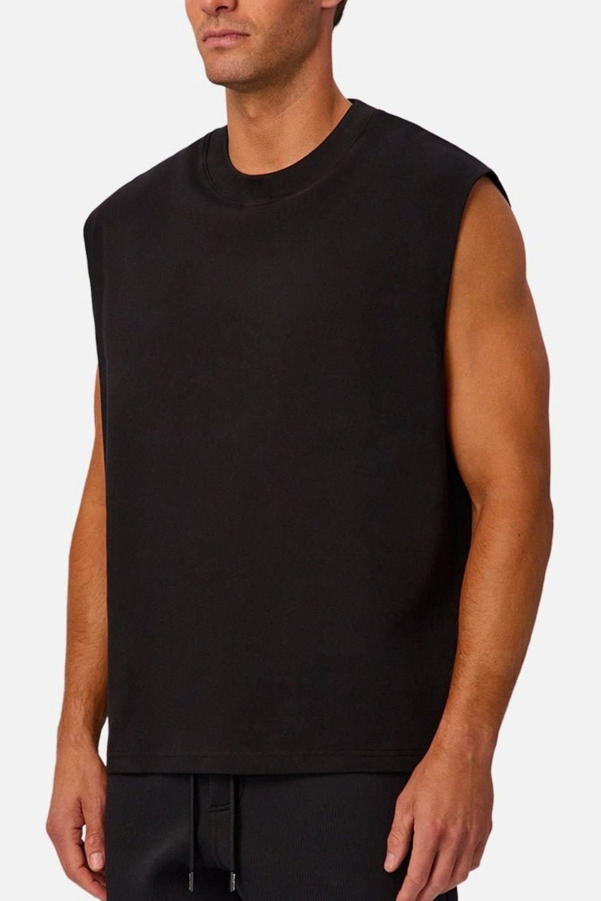 A man wearing the Industrie The Tech Port Sleeveless Tee and black pants stands against a plain light background.