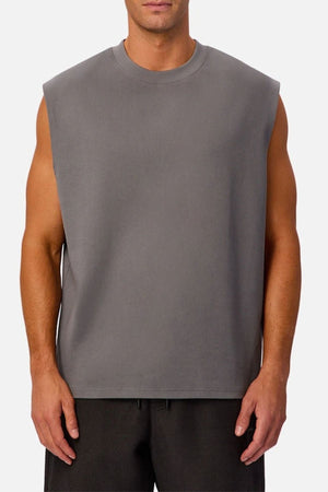 A man stands against a plain white background wearing the Industrie The Tech Port Sleeveless Tee in gray, its relaxed fit and tech material complementing his casual stance as he pairs it with black shorts, arms resting comfortably at his sides.