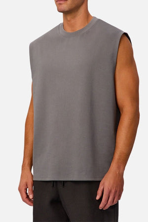 A man wears the Industrie The Tech Port Sleeveless Tee in a relaxed fit with dark pants, standing against a plain, light background.