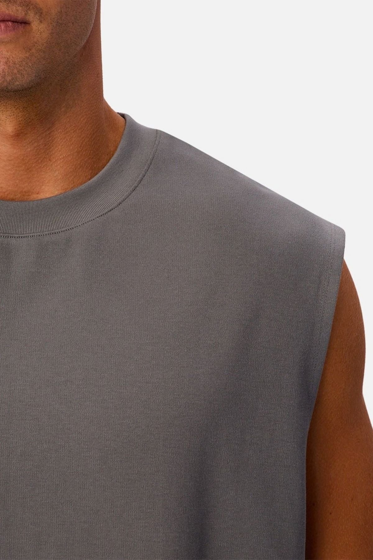 A close-up of a person wearing the Industrie The Tech Port Sleeveless Tee in gray, highlighting part of their neck, shoulder, and upper arm against a plain background. The relaxed fit and technical fabric emphasize comfort and modern style.