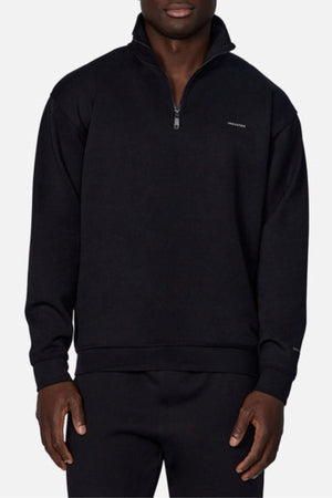 A man in the Industrie The Tech Staunton Track Top and matching black pants, both with a small left chest logo, stands against a plain light background.