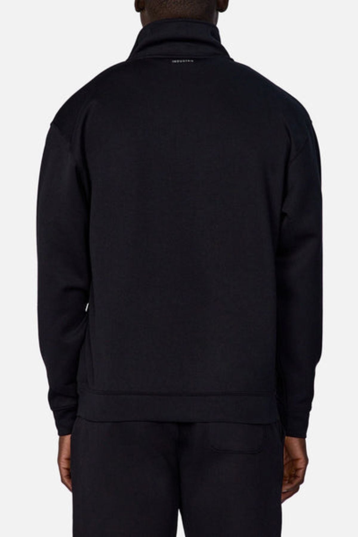 Seen from the back, a person wears the Industrie The Tech Staunton Track Top and matching pants in black. The athletic jacket has a high collar and a small white logo at the top, set against a plain light background.